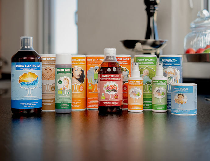 Das Bild zeigt die gesamte Palette der Sojall-Produkte der Firma Heine Gesundheitsversand. DAs Erste Produkt ist eine Flasche aus dunkeln Gals und einem blauen Etikett darauf, Sojall Elektro Kur, daneben stehen sechs größere Pulverdosen. Die erste in braun enthält Sojall Darmil, die Zweite in gelborange enthält Sojall Braunhirse, die Dritte in orange enthält Sojall Vita Power, die Vierte in rot enthält Sojall Sport Natur, die Fünfte in grün enthält Sojall Balance und die Sechste in blau enthält Sojall Royal. Daneben eine kleinere Pulverdose in hellblau mit Sojal Makal. In der vordersten Reihe stehen noch Sojall Topil, Sojall Trinko und zwei Sojall Sprays.