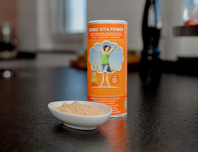 Das Bild zeigt eine orangene Pulverdose von Sojall Vita Power. Davor steht eine kleine Schale mit pulver aus der Dose.